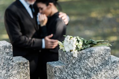 selective focus of bouquet on tombstone near man hugging woman  clipart