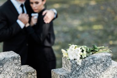 selective focus of flowers on tomb near senior man hugging woman  clipart
