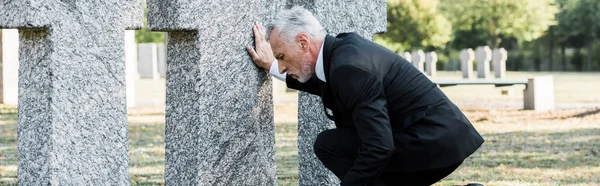 墓石の近くに座っているスーツを着た動揺した先輩のパノラマショット — ストック写真