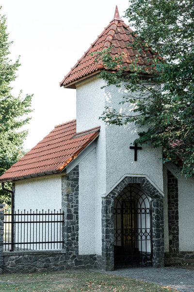 green trees near christian church with red roof and metallic fence 