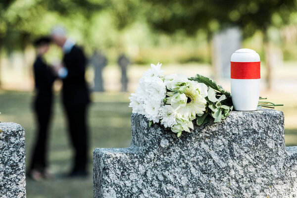 selective focus of bouquet of white flowers and cemetery urn on tombstone