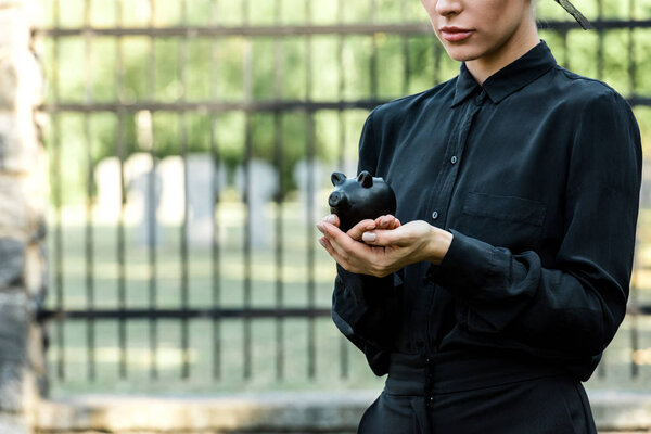 cropped view of woman holding black piggy bank near metallic fence 