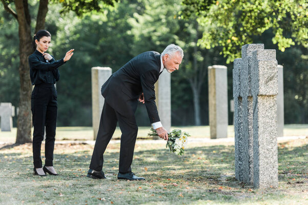 man with grey hair putting flowers near tombstones and woman 