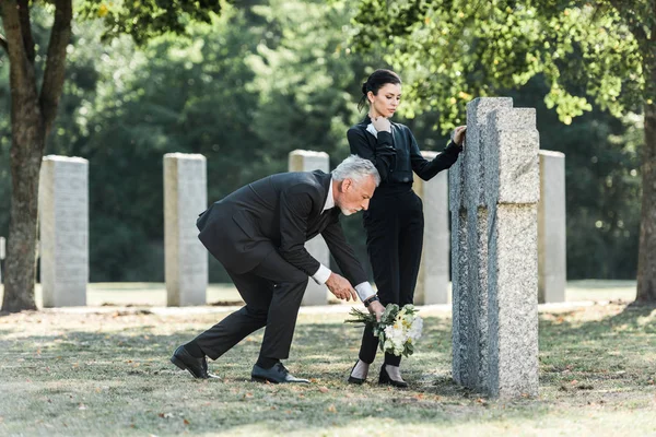 Senior Man Sätta Blommor Nära Gravstenar Och Vacker Kvinna — Stockfoto