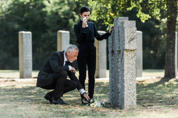 man with grey hair putting flowers near tombstones and crying woman 