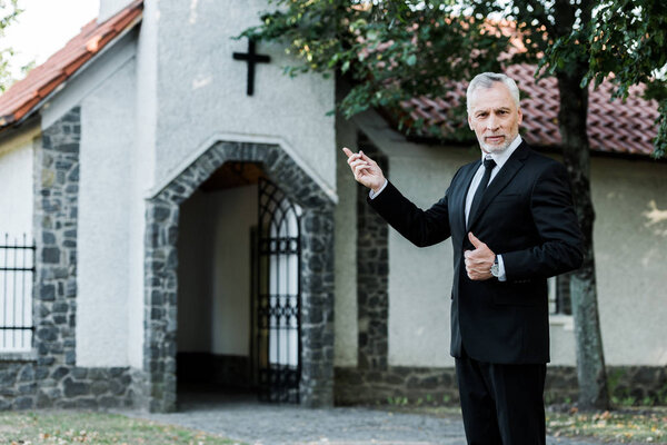 senior man showing thumb up and pointing with finger at church 