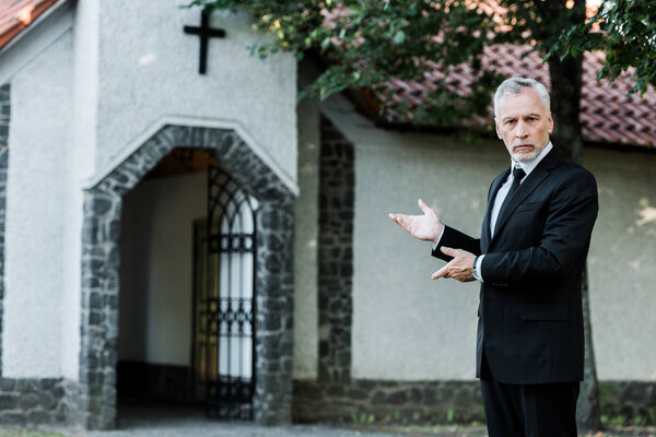 handsome senior man in suit gesturing near church 