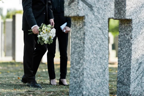 墓の近くに花を持つ女性の近くに立っている男のトリミングされたビュー — ストック写真