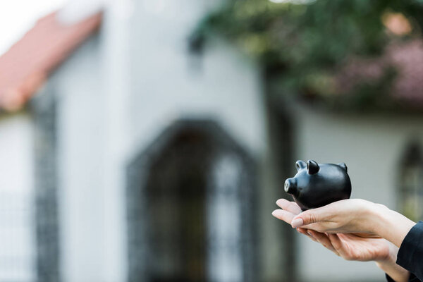 cropped view of woman holding black piggy bank near building