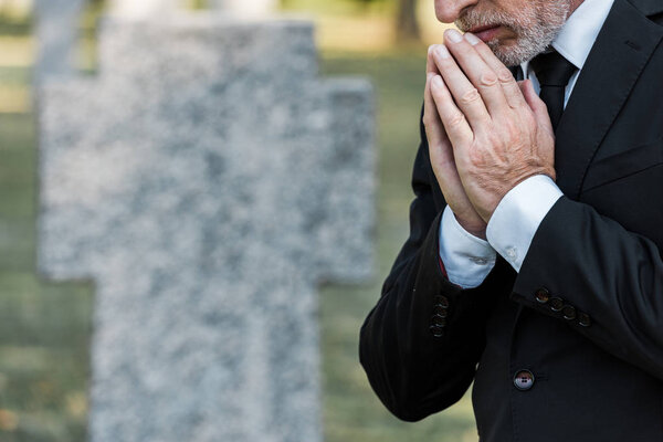 cropped view of senior man standing with praying hands 