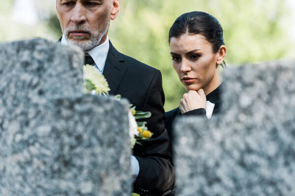 selective focus of upset senior man and attractive woman on graveyard 