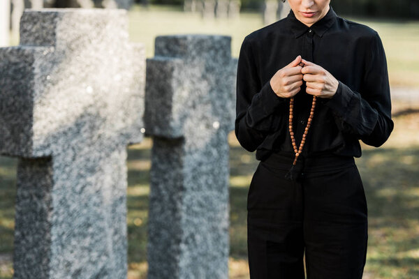 cropped view of woman holding rosary beads near tombstones 