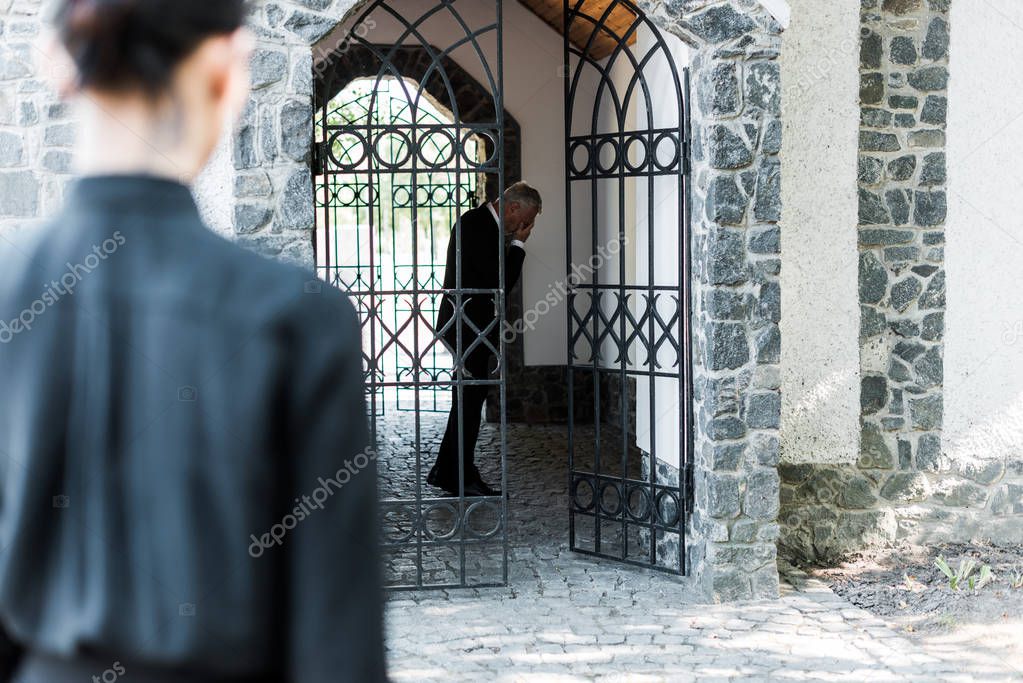 selective focus of upset man covering face in building near woman 