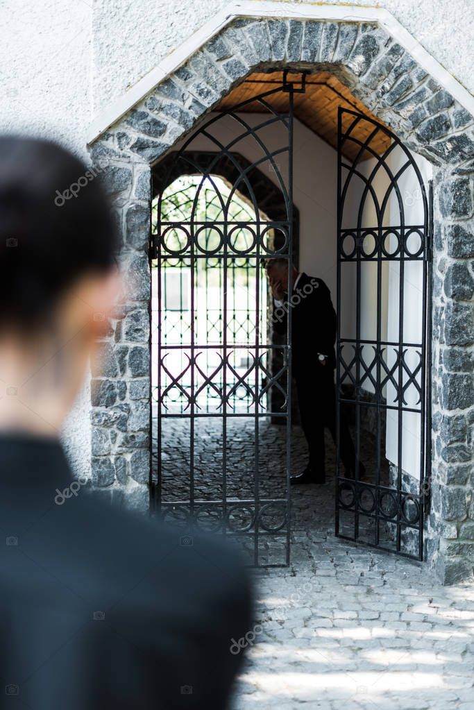 selective focus of sad senior man standing in building near woman in cemetery 