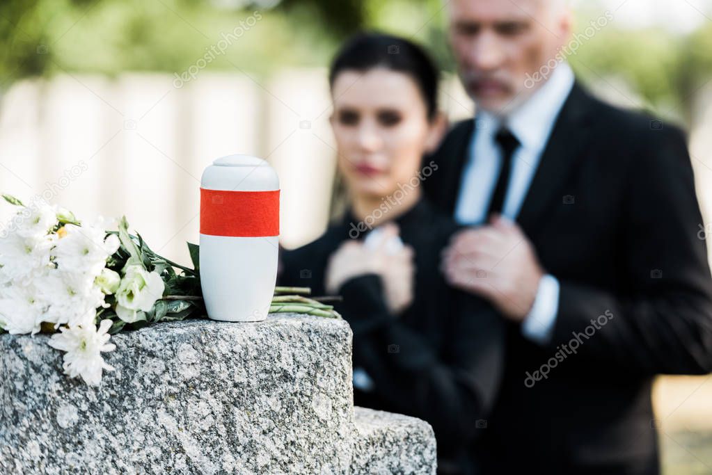 selective focus of white flowers near mortuary urn and two people 