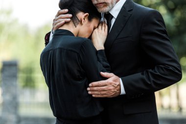 cropped view of sad elderly man embracing woman on funeral  clipart