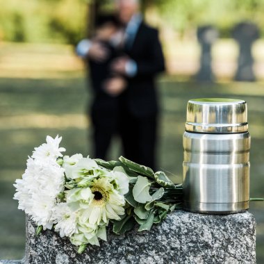 selective focus of white flowers and mortuary urn on tombstone clipart