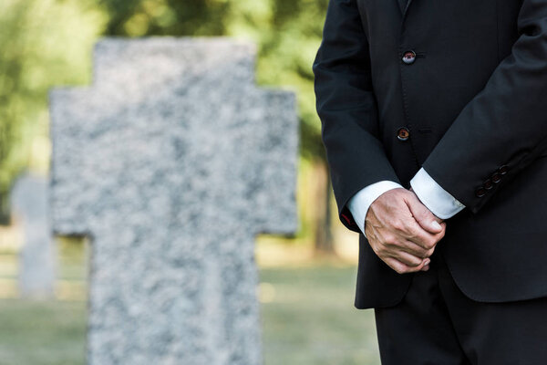 cropped view of elderly man standing near tombs with clenched hands 