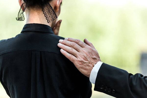 cropped view of elderly man touching woman on funeral 