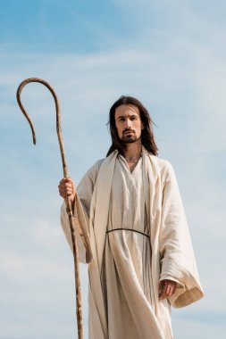  çölde mavi gökyüzüne karşı ahşap baston tutan İsa cüppe adam 
