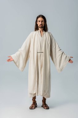 handsome bearded man in jesus robe standing with outstretched hands on grey clipart