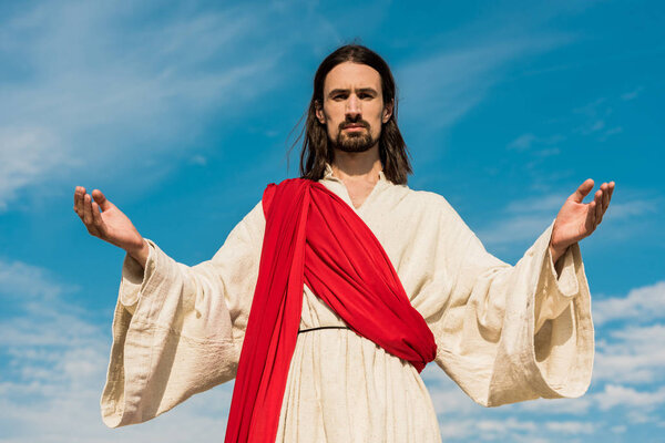 bearded jesus with outstretched hands against blue sky 