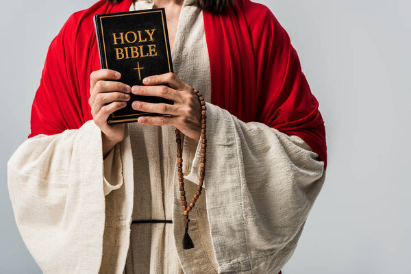 cropped view of man holding holy bible and rosary breads isolated on grey 