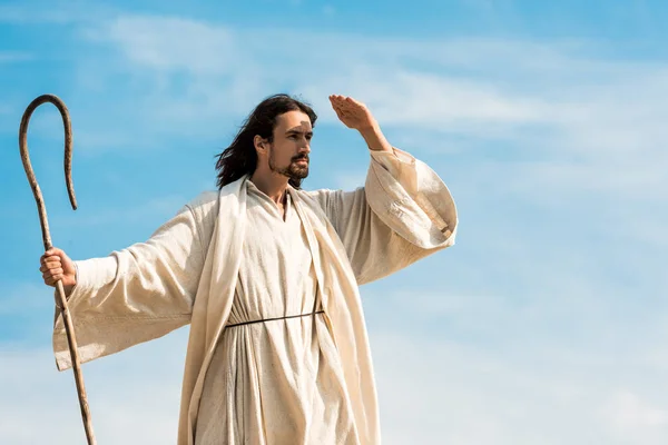 man in jesus robe holding cane against blue sky