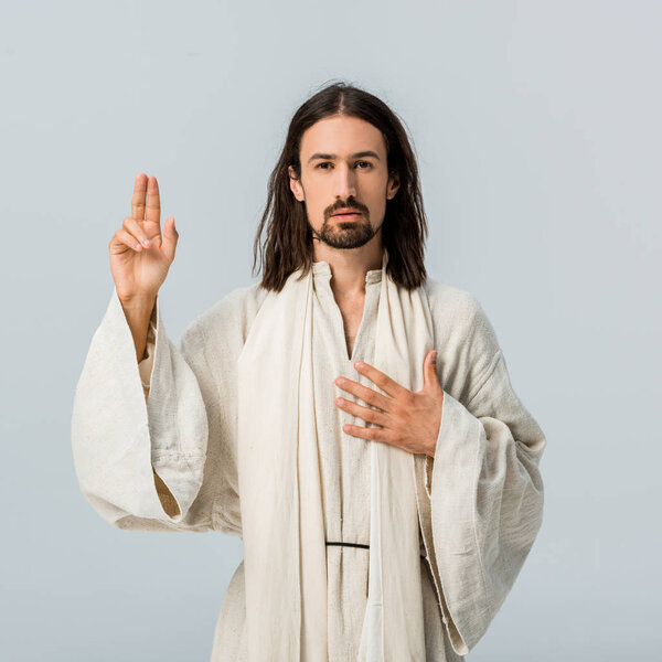 handsome man praying with hand on chest isolated on grey 