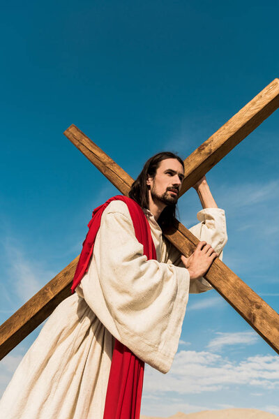 low angle view of jesus holding cross against blue sky 