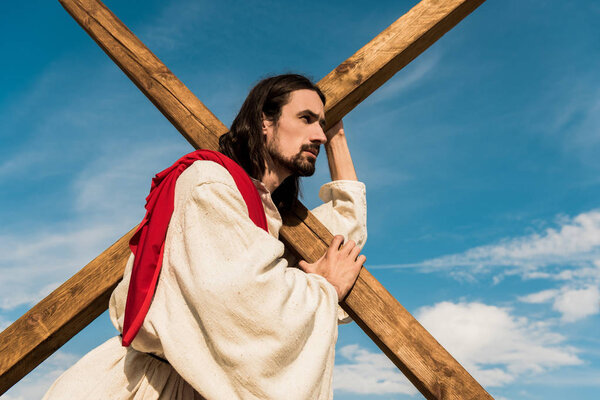 low angle view of bearded man holding cross against blue sky 