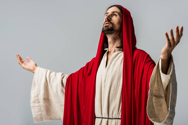 bearded man in red hood praying with outstretched hands isolated on grey 