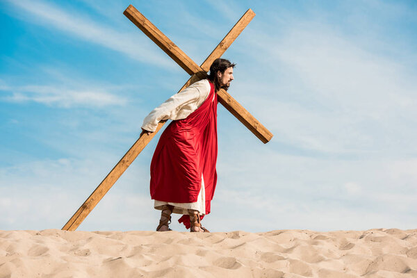 bearded man in wreath walking with cross in desert 