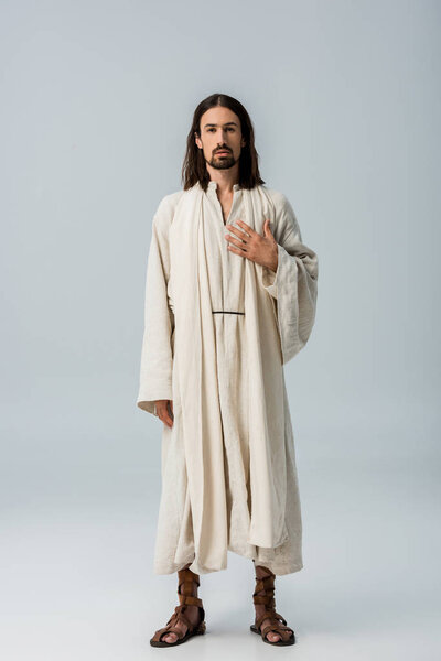 красивый мужчина, стоящий с рукой на груди на сером
 