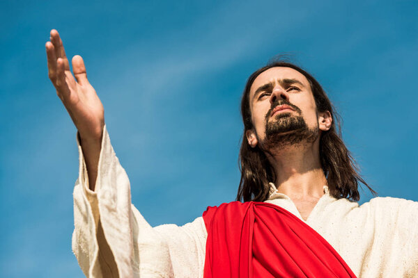 low angle view of man with outstretched hand against blue sky 