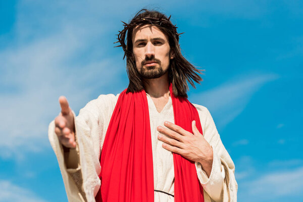 selective focus of jesus in wreath gesturing against blue sky 