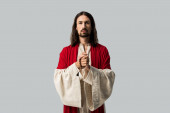 pohledný muž modlící se sevřenými dlaněmi izolovanými na šedé
