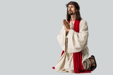 handsome man in wreath praying on knees isolated on grey clipart