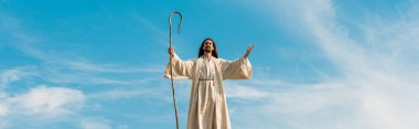 panoramic shot of jesus with outstretched hands holding wooden cane against sky clipart