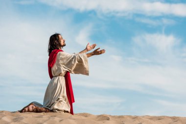 İsa gökyüzüne karşı çölde kum üzerinde dizüzerinde dua 