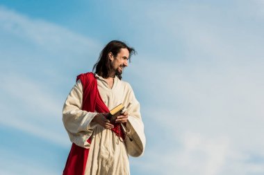 jesus holding cross and holy bible against sky with clouds  clipart