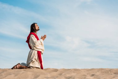 man praying on knees in desert on golden sand  clipart