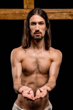 jesus with bloody hands standing near wooden cross isolated on black  clipart