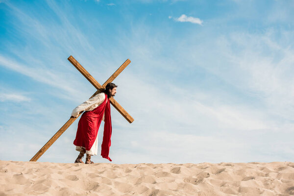 bearded man walking with wooden cross in desert 