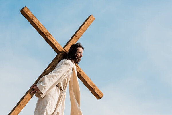 bearded jesus holding wooden cross against sky 