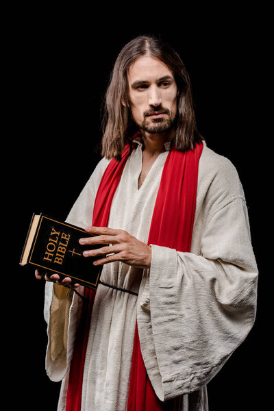 handsome man in jesus robe holding holy bible isolated on black 