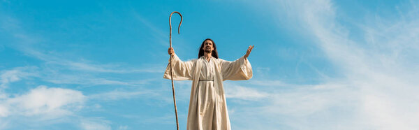 panoramic shot of jesus with outstretched hands holding wooden cane against sky