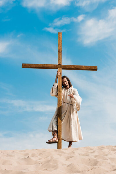 bearded man standing with wooden cross in desert 