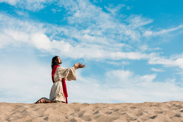 jesus praying on knees in desert against sky 