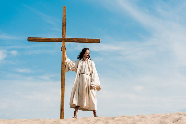 handsome bearded man standing with wooden cross in desert 